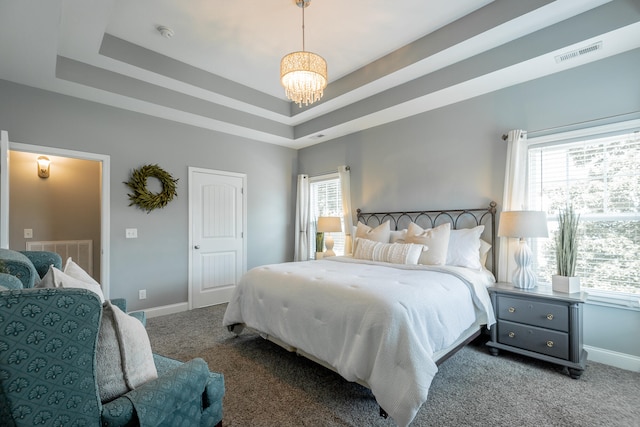 carpeted bedroom featuring a raised ceiling, multiple windows, and an inviting chandelier