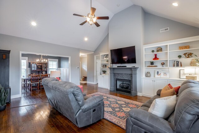 living room with high vaulted ceiling, ceiling fan with notable chandelier, a tiled fireplace, and dark hardwood / wood-style flooring