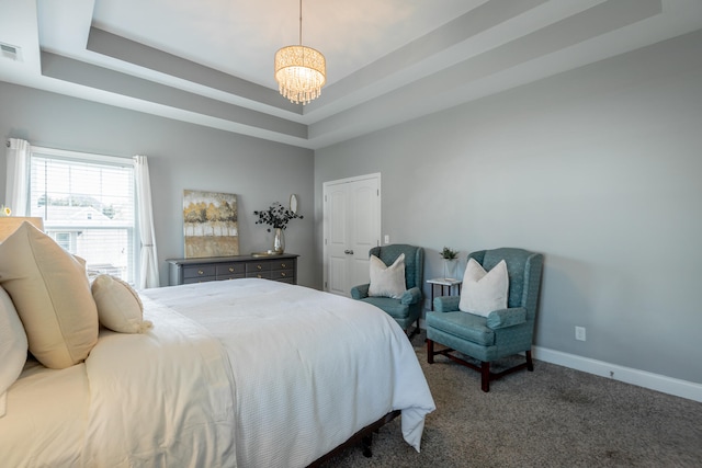 bedroom with a raised ceiling, dark colored carpet, and a chandelier