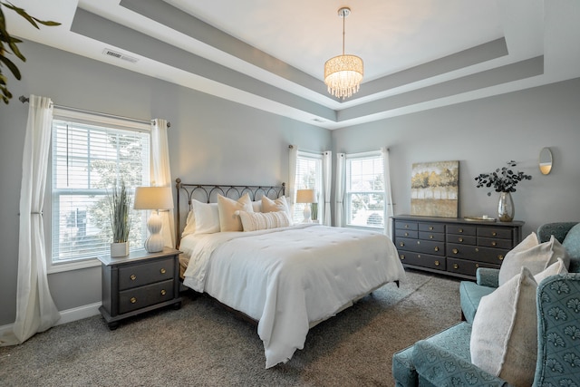 carpeted bedroom featuring a raised ceiling and a chandelier