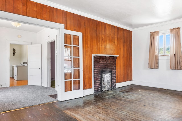 unfurnished living room featuring wooden walls, a fireplace, dark hardwood / wood-style floors, ornamental molding, and washing machine and dryer