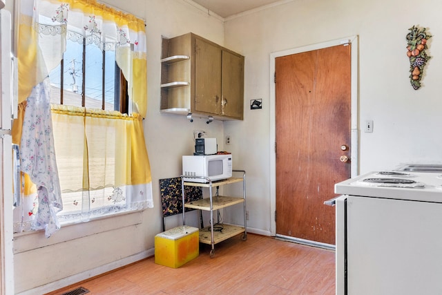 kitchen with a wealth of natural light, crown molding, white appliances, and light hardwood / wood-style floors