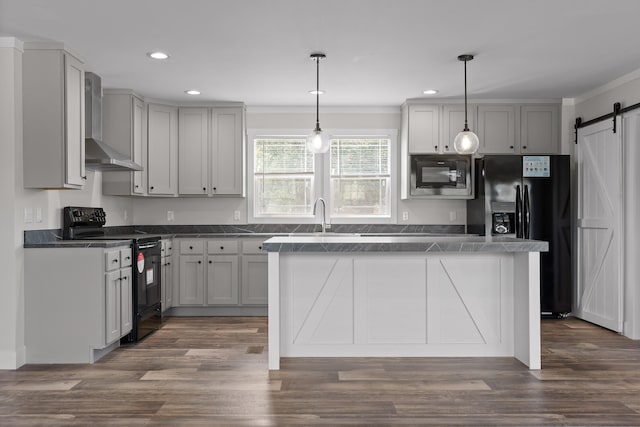 kitchen featuring gray cabinetry, black appliances, wall chimney range hood, and a barn door