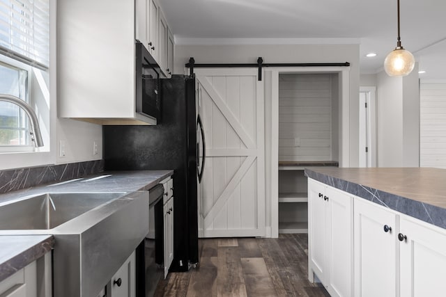 kitchen with a barn door, dark hardwood / wood-style flooring, decorative light fixtures, black appliances, and white cabinetry