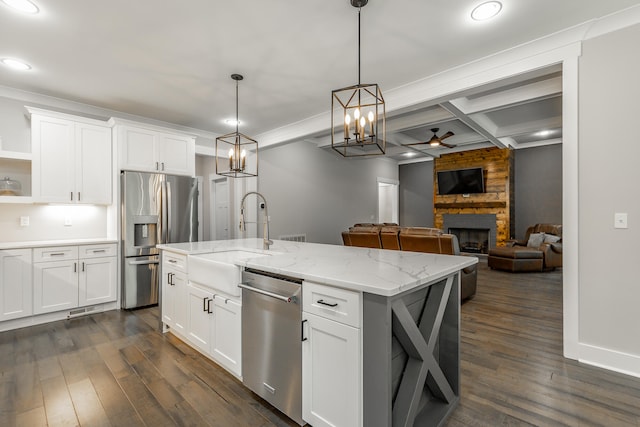 kitchen with ceiling fan with notable chandelier, appliances with stainless steel finishes, a kitchen island with sink, a large fireplace, and white cabinetry