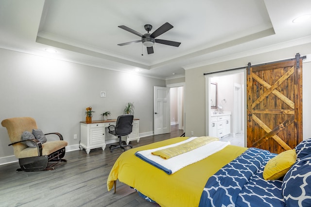 bedroom featuring wood-type flooring, a tray ceiling, ensuite bath, a barn door, and ceiling fan