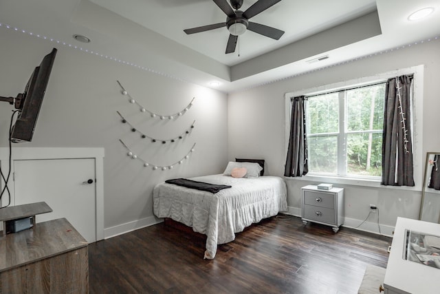 bedroom with dark wood-type flooring, ceiling fan, and a raised ceiling