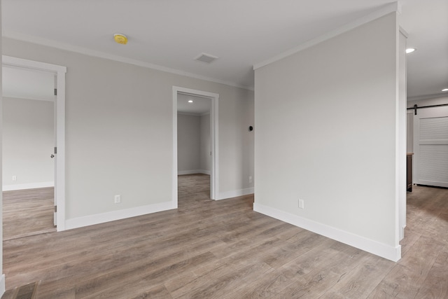 spare room with ornamental molding, light wood-type flooring, and a barn door