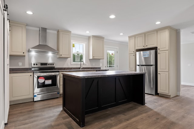 kitchen featuring stainless steel appliances, cream cabinetry, a barn door, and wall chimney range hood