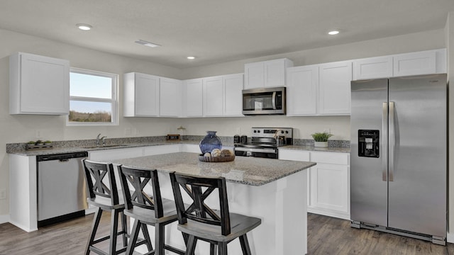 kitchen featuring a center island, hardwood / wood-style floors, appliances with stainless steel finishes, light stone counters, and white cabinetry