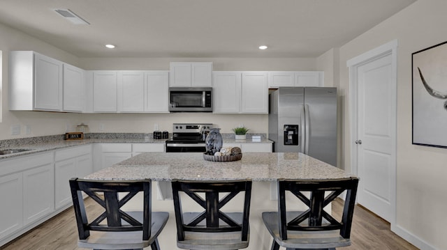 kitchen with light wood-type flooring, stainless steel appliances, a center island, light stone countertops, and a breakfast bar