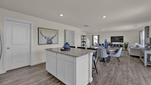 kitchen with a center island, light stone countertops, white cabinets, and light hardwood / wood-style floors