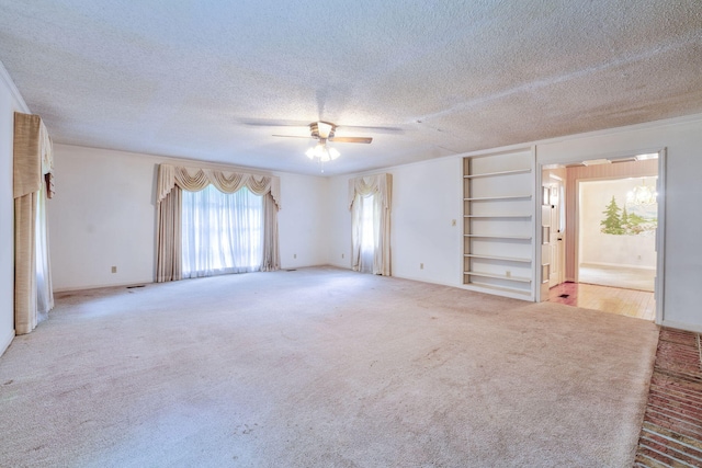 unfurnished room featuring light colored carpet, a textured ceiling, built in shelves, and ceiling fan