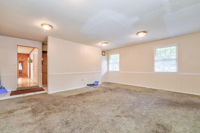 unfurnished room featuring a wealth of natural light, wooden walls, carpet floors, and a textured ceiling