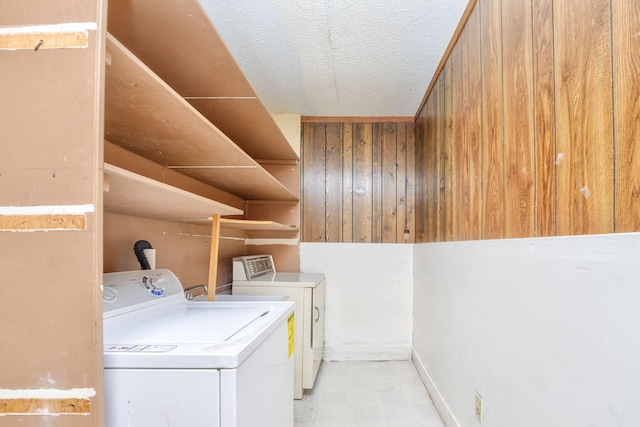 laundry room featuring separate washer and dryer, a textured ceiling, and wood walls