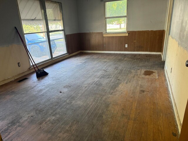 empty room with dark wood-type flooring, a wealth of natural light, and wooden walls