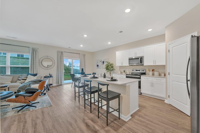 kitchen featuring light wood-type flooring, appliances with stainless steel finishes, white cabinetry, a kitchen breakfast bar, and a kitchen island with sink