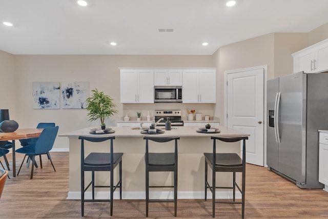 kitchen with white cabinets, light hardwood / wood-style flooring, stainless steel appliances, an island with sink, and a breakfast bar area