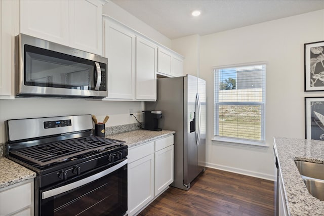 kitchen with appliances with stainless steel finishes, white cabinetry, light stone countertops, and dark hardwood / wood-style floors