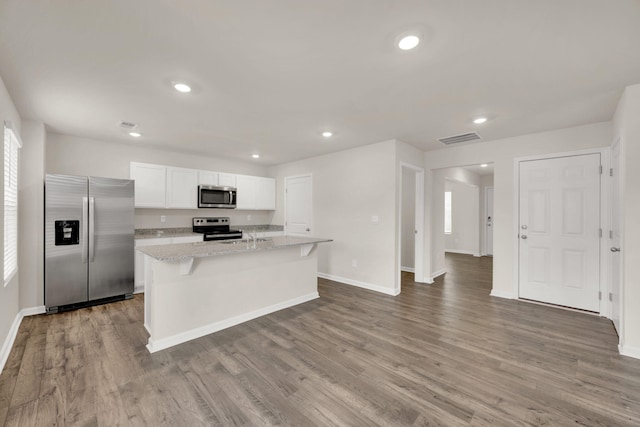 kitchen with visible vents, wood finished floors, white cabinets, stainless steel appliances, and a kitchen island with sink
