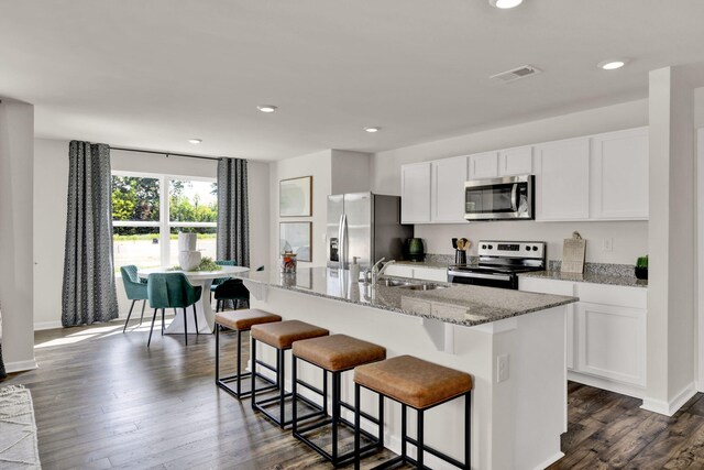 kitchen with dark wood-type flooring, a kitchen breakfast bar, a kitchen island with sink, and stainless steel appliances