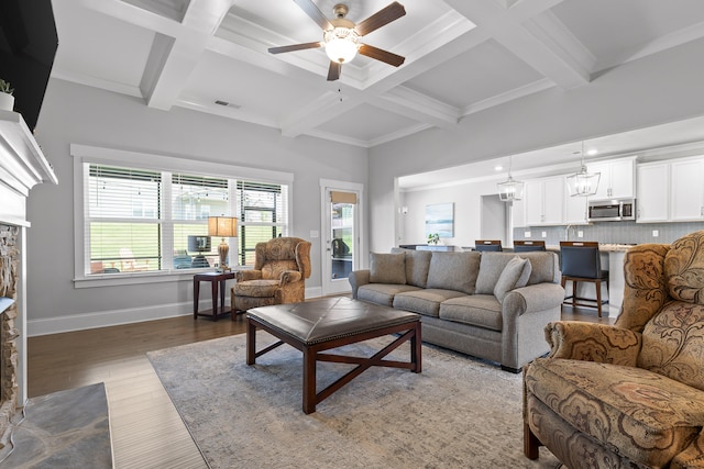 living room featuring ceiling fan with notable chandelier, plenty of natural light, wood-type flooring, and beam ceiling