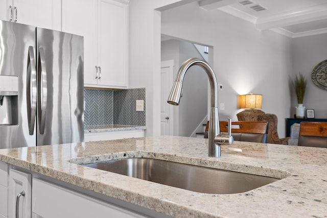 kitchen with stainless steel refrigerator with ice dispenser, white cabinetry, sink, and light stone countertops