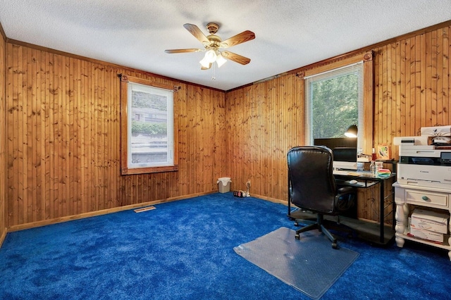 carpeted office with wooden walls, ceiling fan, and a healthy amount of sunlight
