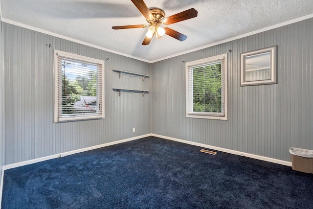 empty room with a textured ceiling, carpet, ceiling fan, and crown molding