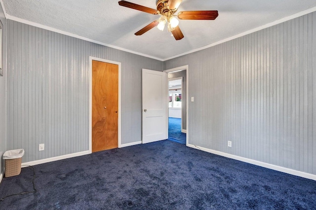 unfurnished bedroom with crown molding, a textured ceiling, dark carpet, a ceiling fan, and baseboards