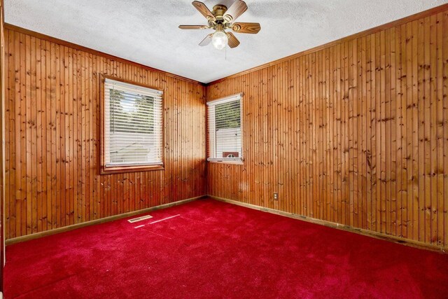 carpeted spare room featuring wooden walls, a textured ceiling, ceiling fan, and visible vents