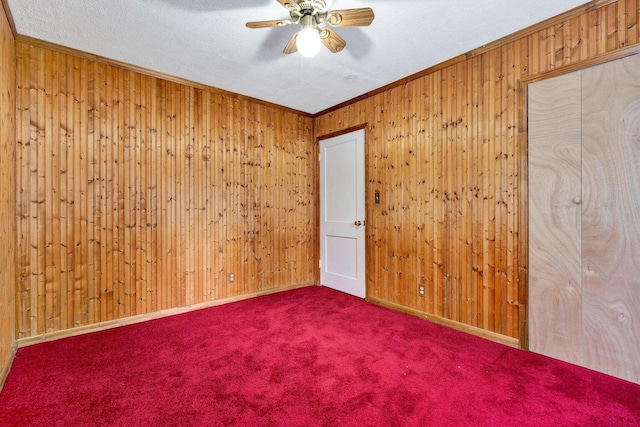 carpeted spare room with ornamental molding, a textured ceiling, ceiling fan, and wooden walls