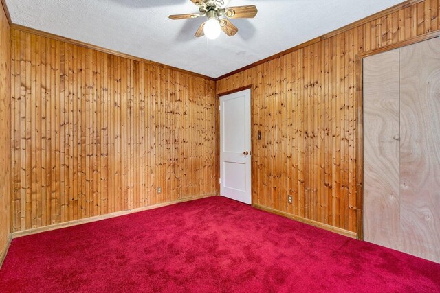 carpeted empty room with crown molding, wood walls, baseboards, and ceiling fan