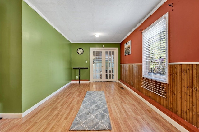 spare room featuring ornamental molding, wooden walls, french doors, and light hardwood / wood-style floors