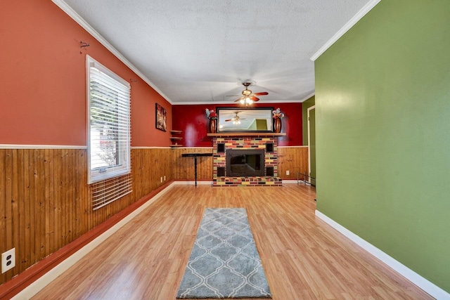 unfurnished living room featuring ceiling fan, wooden walls, wood-type flooring, and a brick fireplace