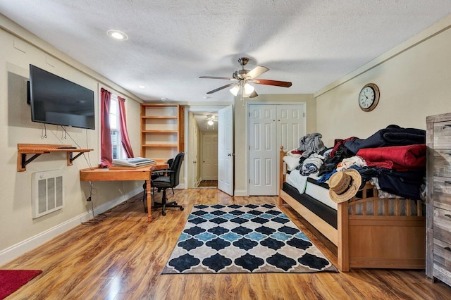 bedroom with a ceiling fan, a textured ceiling, visible vents, wood finished floors, and baseboards