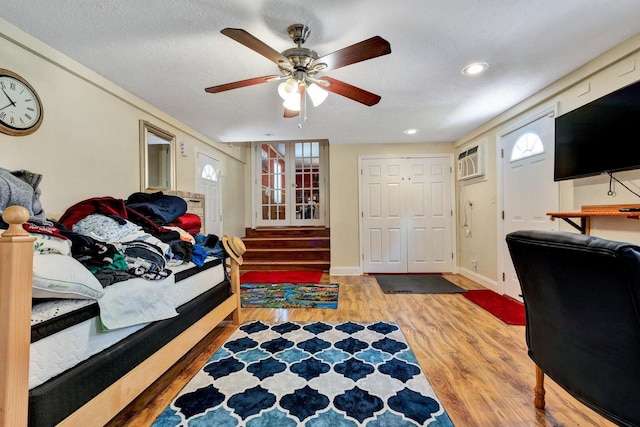 bedroom featuring a wall mounted AC, a textured ceiling, wood-type flooring, ceiling fan, and a closet