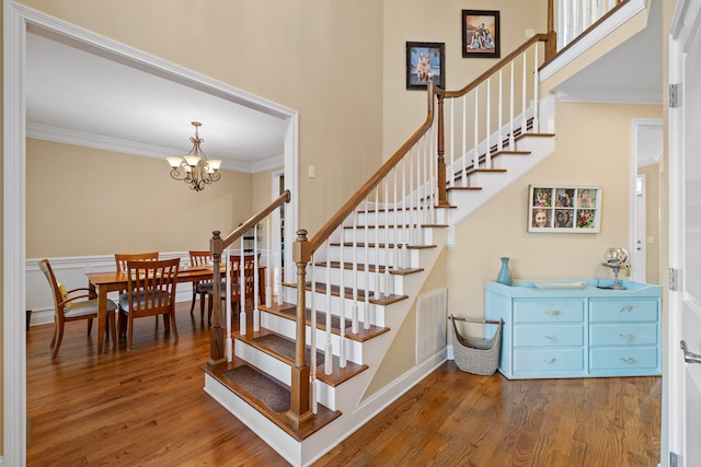 stairway featuring ornamental molding, wood-type flooring, and an inviting chandelier