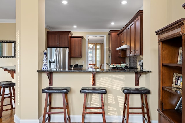 kitchen featuring a kitchen bar, decorative backsplash, dark stone counters, and stainless steel refrigerator with ice dispenser