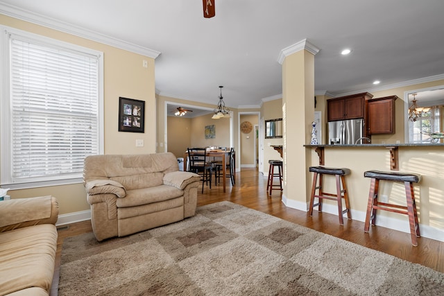 living room with ceiling fan with notable chandelier, dark wood-type flooring, and crown molding