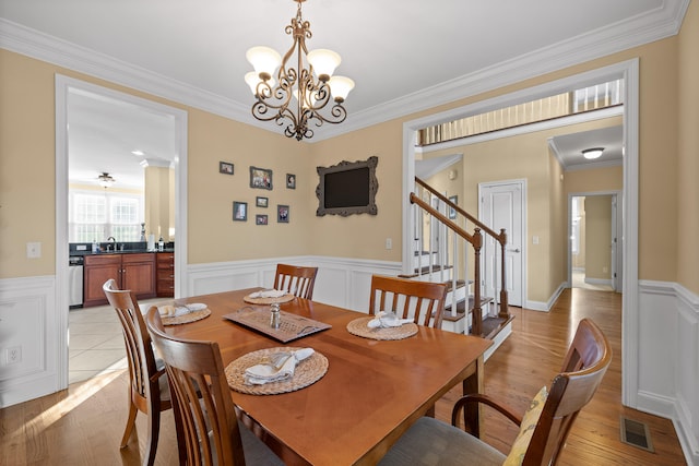 dining room with light wood-type flooring, ornamental molding, a chandelier, and sink