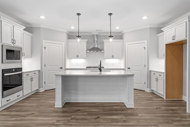 kitchen with stainless steel oven, white cabinetry, a kitchen island with sink, wall chimney range hood, and black microwave