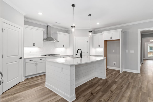 kitchen with wall chimney exhaust hood, white cabinetry, backsplash, a kitchen island with sink, and stainless steel gas stovetop