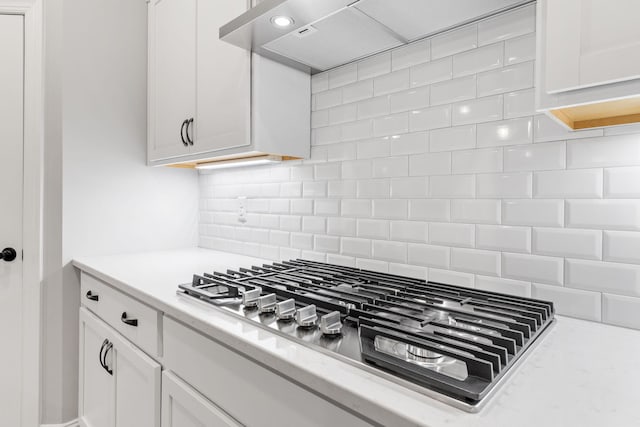 kitchen with wall chimney range hood, tasteful backsplash, stainless steel gas stovetop, and white cabinetry