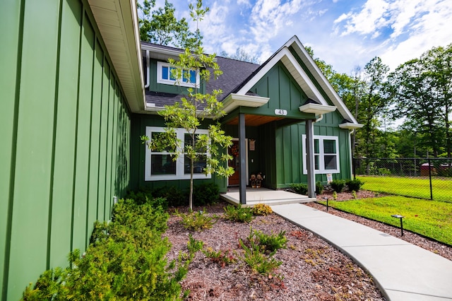 exterior space with a lawn, board and batten siding, a shingled roof, and fence