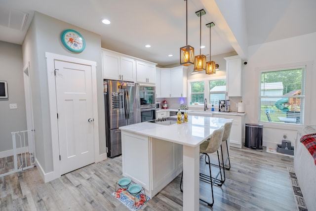 kitchen featuring a breakfast bar area, light countertops, light wood-style flooring, white cabinets, and stainless steel appliances