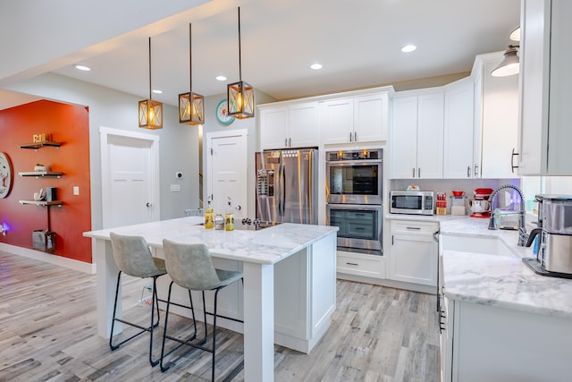 kitchen with light stone countertops, light wood-type flooring, appliances with stainless steel finishes, a kitchen island, and white cabinetry