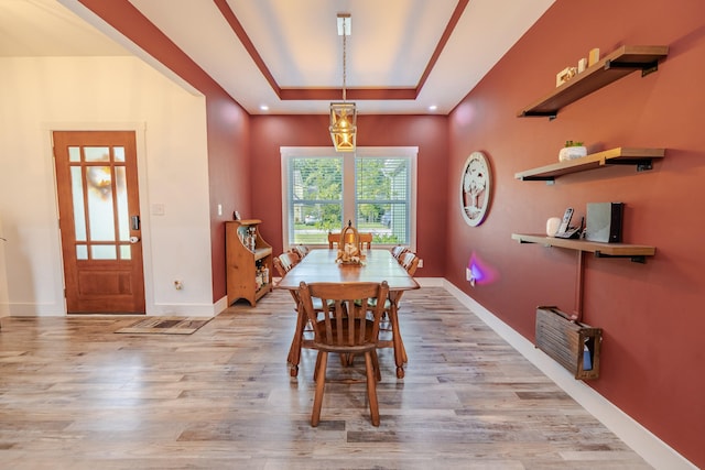 dining area with light wood-type flooring and a tray ceiling