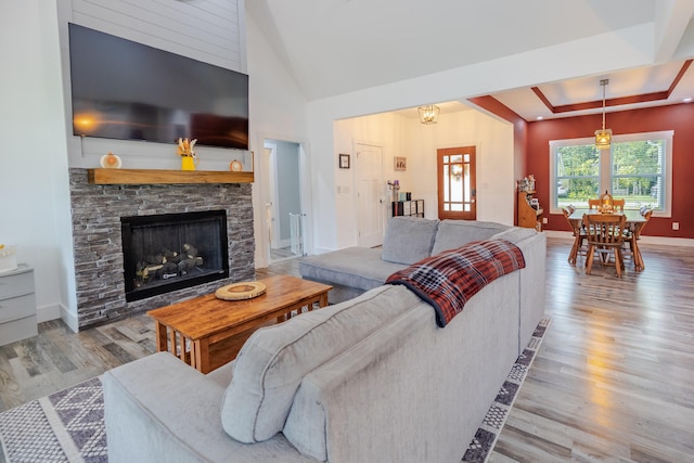 living room with a raised ceiling, wood finished floors, a fireplace, baseboards, and vaulted ceiling
