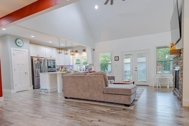 living area featuring french doors, high vaulted ceiling, light wood-style flooring, and a fireplace